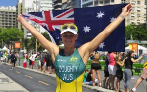 Australian Paralympian Kate Doughty standing with her arms outstretched above her head holding the Australian flag