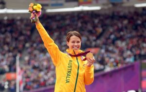 Kelly Cartwright standing on the medal podium holding a gold medal