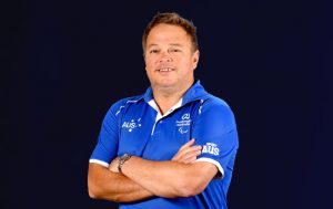 Profile photo of Australian Wheelchair Basketball coach Craig Friday in a blue polo, with his arms folded across his chest, smiling at the camera