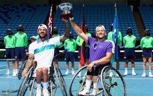 Australian wheelchair tennis players Heath Davidson and Dylan Alcott holding a trophy above their heads and smiling