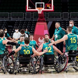 A group wheelchair athletes form a huddle at the end of a basketball game