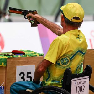 A male representing Australia in a shooting competition. He is aiming at a target