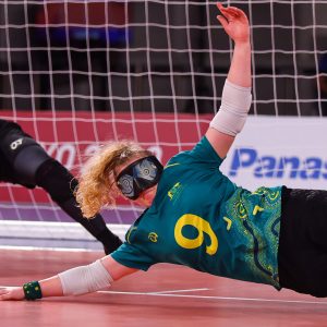 A female Australian Goalball player diving to the left of the image to block a goal