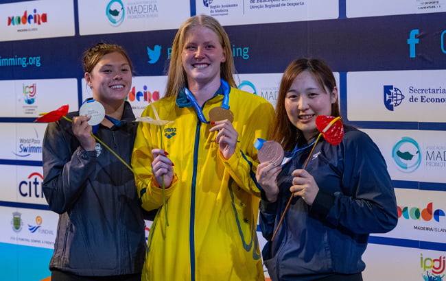 Australian Paralympian Katja Dedekind holding a gold medal. She is in between 2 other female swimmers holding medals.