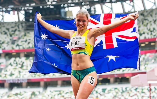 Australian Paralympian Isis Holt holding the Australian flag over her shoulders and smiling.