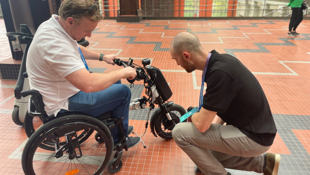A man testing out a mobility device with another man helping.