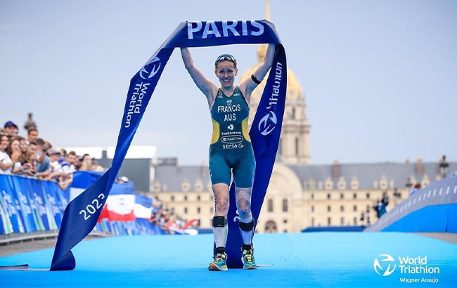 Australian Para-triathlon athlete Anu Francis crossing a finishing line and holding the ribbon above her head in celebration.