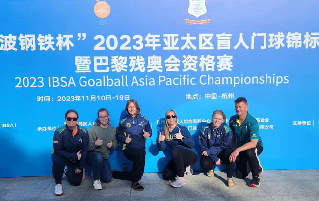 The Aussie Belles kneeling in front of a sign that reads '2023 IBSA Goalball Asia Pacific Championships'